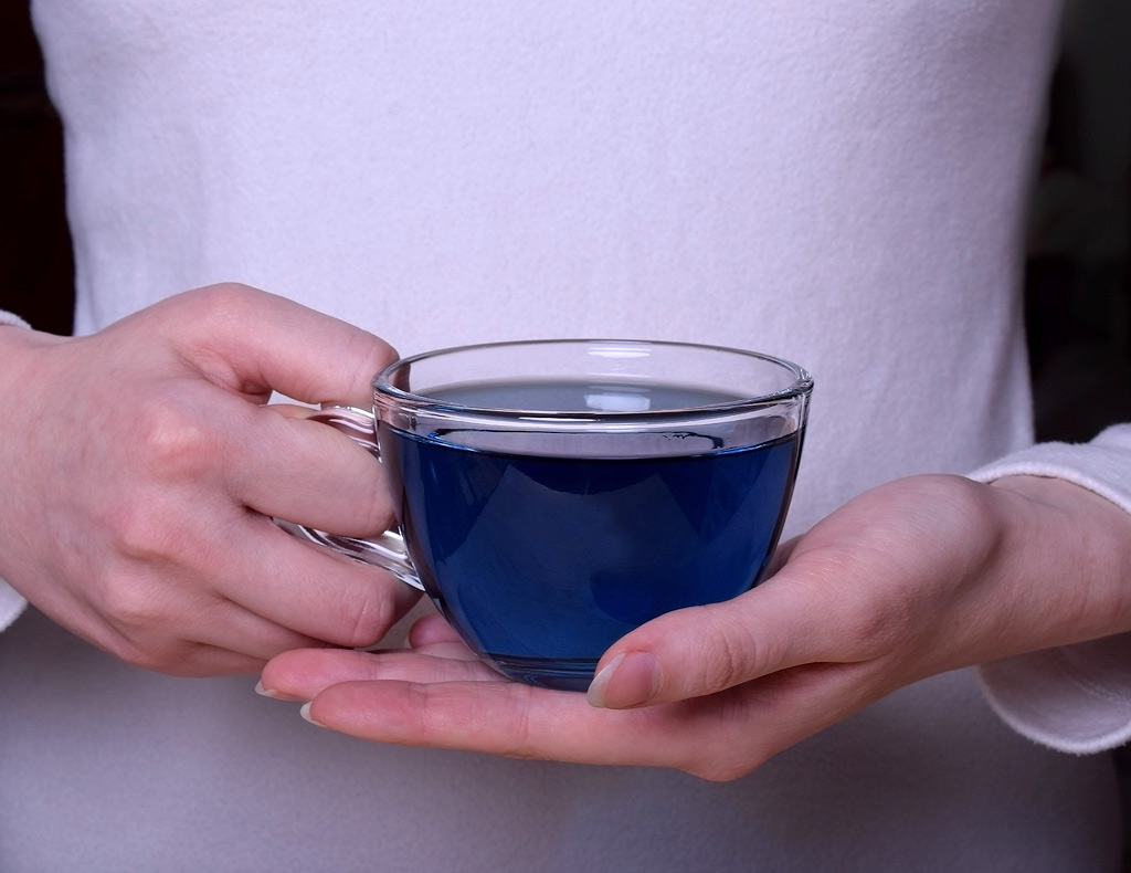 Eine Frau hält eine Tasse blauen Tee vor ihren Bauch.